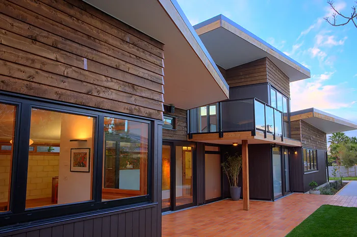 Home with vertical timber cladding, large windows and a balcony at dusk